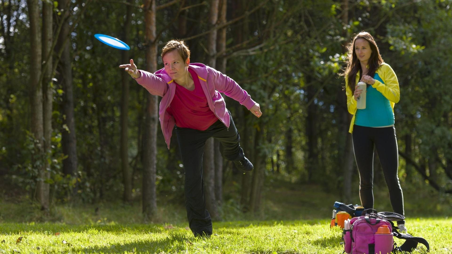 Zwei junge Frauen spielen auf einer Wiese am Waldrand Frisbee. Zwei junge Frauen spielen auf einer Wiese am Waldrand Frisbee.