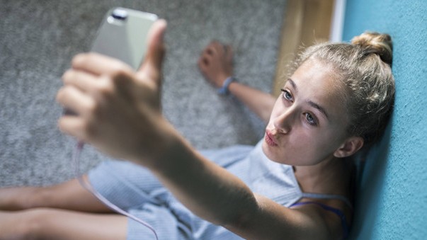 Ein Mädchen sitzt in ihrem Zimmer auf dem Boden und macht "Selfies" 