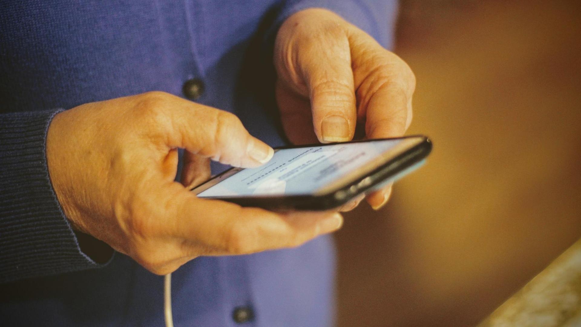 Die Hände einer älteren Person bedienen ein Smartphone. Die Hände einer älteren Person bedienen ein Smartphone.
