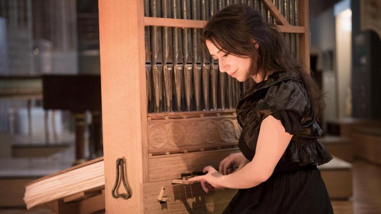 Eine Frau mit braunen Haaren im schwarzen Kleid sitzt vor einer kleinen historischen Orgel