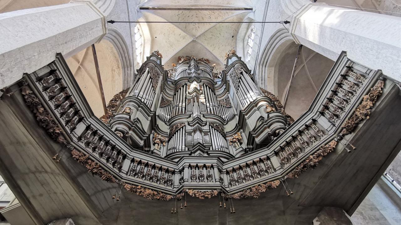 Blick senkrecht von unten nach oben in einer Kirche, wo über einer Brüstung zwischen mächtigen Steinsäulen die Edelstahl-Pfeifen einer Kirchenorgel hängen. Blick senkrecht von unten nach oben in einer Kirche, wo über einer Brüstung zwischen mächtigen Steinsäulen die Edelstahl-Pfeifen einer Kirchenorgel hängen.