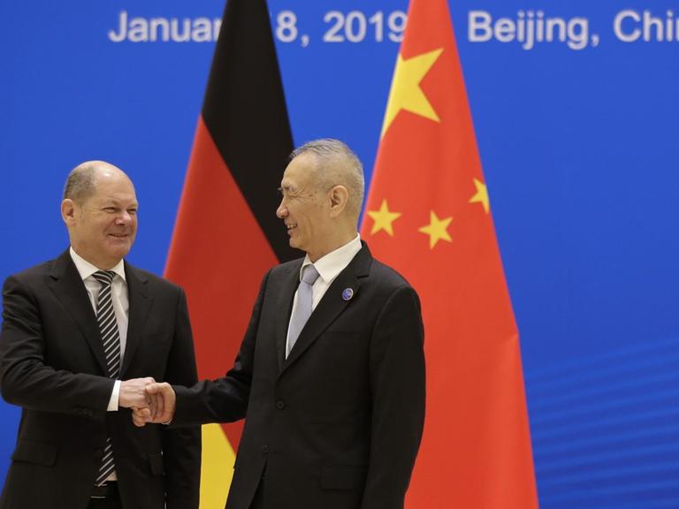 Der deutsche Finanzminister Olaf Scholz gibt dem chinesischen Vize-Premierminister Liu He vor den deutschen und chinesischen Flaggen die Hand.