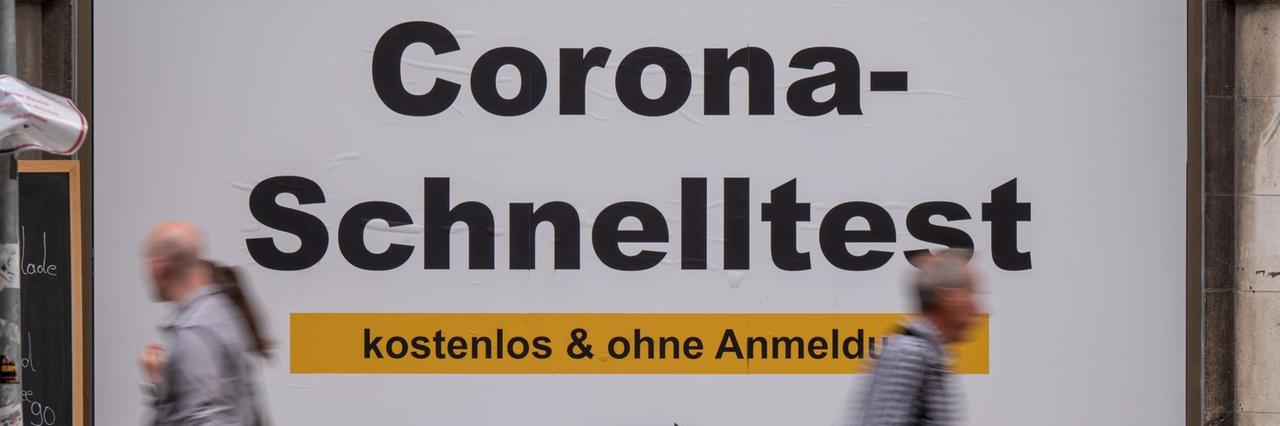 Passanten gehen in der Fußgängerzone in der Innenstadt an einem Plakat mit der Aufschrift „Corona-Schnelltest - kostenlos und ohne Anmeldung“ vorbei. Passanten gehen in der Fußgängerzone in der Innenstadt an einem Plakat mit der Aufschrift „Corona-Schnelltest - kostenlos und ohne Anmeldung“ vorbei.