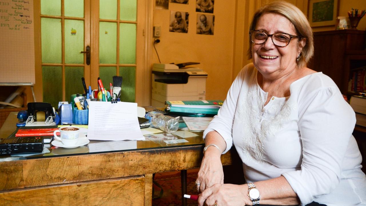 Eine Frau in weißem Oberteil und mit Brille schaut lächelnd in die Kamera. Eine Frau in weißem Oberteil und mit Brille schaut lächelnd in die Kamera.
