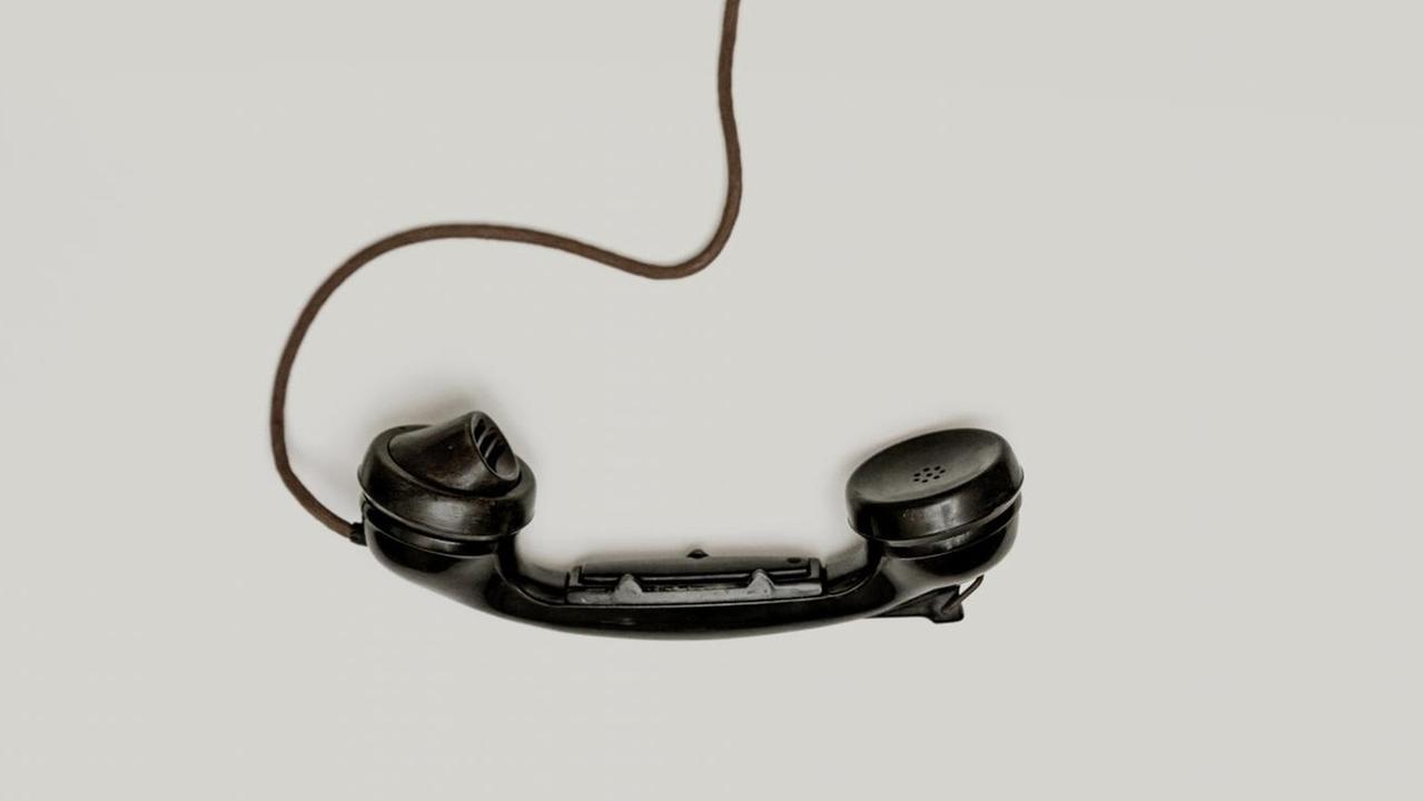 Ein alter Telefonhörer hängt an der Strippe auf grauem Hintergrund.