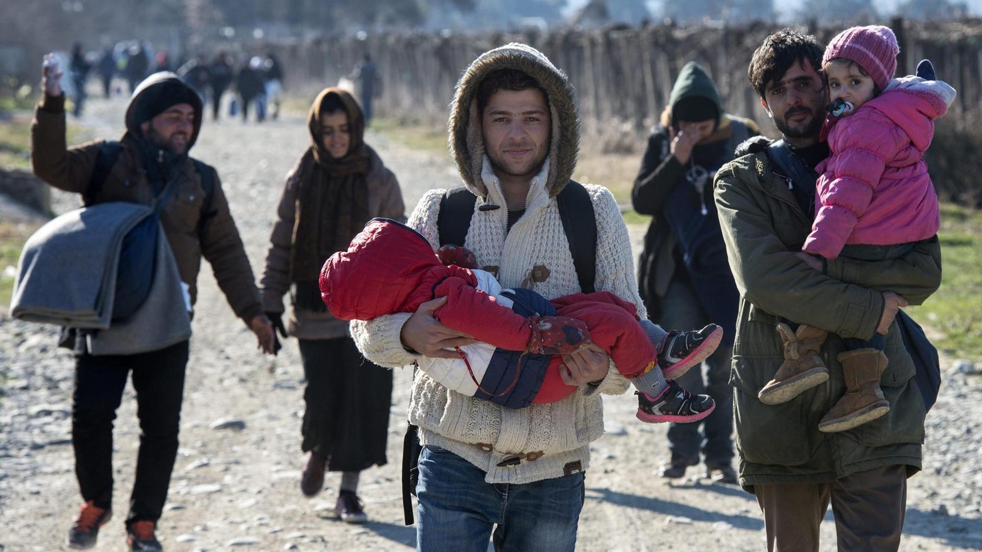 Flüchtlinge mit Kindern auf dem Arm gehen in Mazedonien eine Straße entlang Flüchtlinge mit Kindern auf dem Arm gehen in Mazedonien eine Straße entlang
