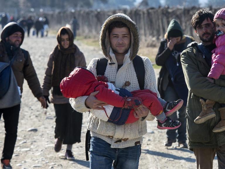 Flüchtlinge mit Kindern auf dem Arm gehen in Mazedonien eine Straße entlang
