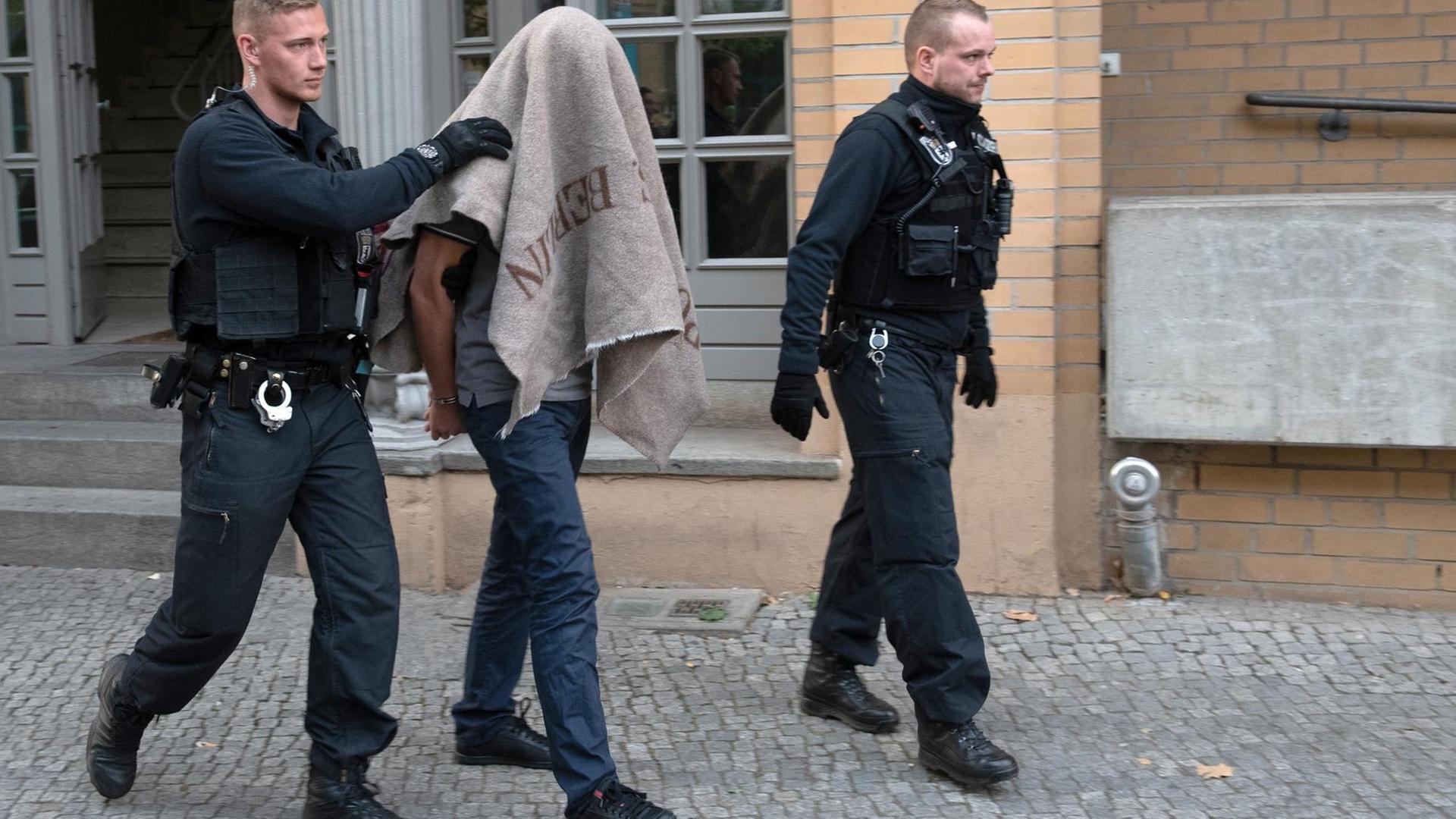 Zwei Polizisten führen einen verdächtigen Mann nach einer Razzia gegen kriminelle Mitglieder arabischer Großfamilien in Berlin ab. Zwei Polizisten führen einen verdächtigen Mann nach einer Razzia gegen kriminelle Mitglieder arabischer Großfamilien in Berlin ab.