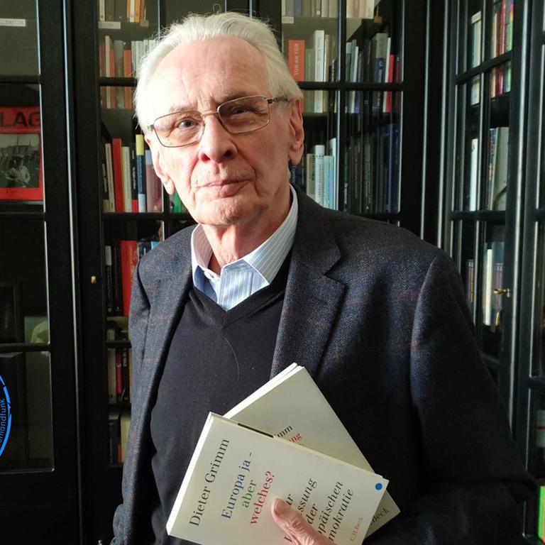 Der Verfassungsrechtler Dieter Grimm steht in einer Bibliothek und hält sein Buch "Europa ja - aber welches?"