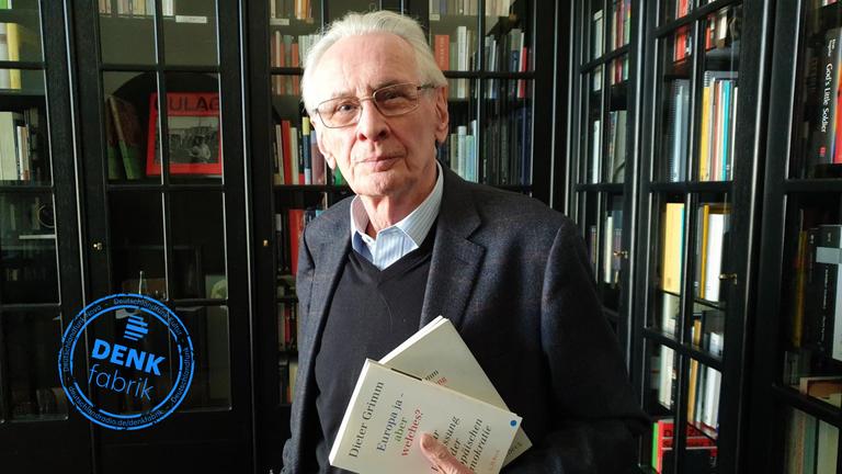 Der Verfassungsrechtler Dieter Grimm steht in einer Bibliothek und hält sein Buch "Europa ja - aber welches?"
