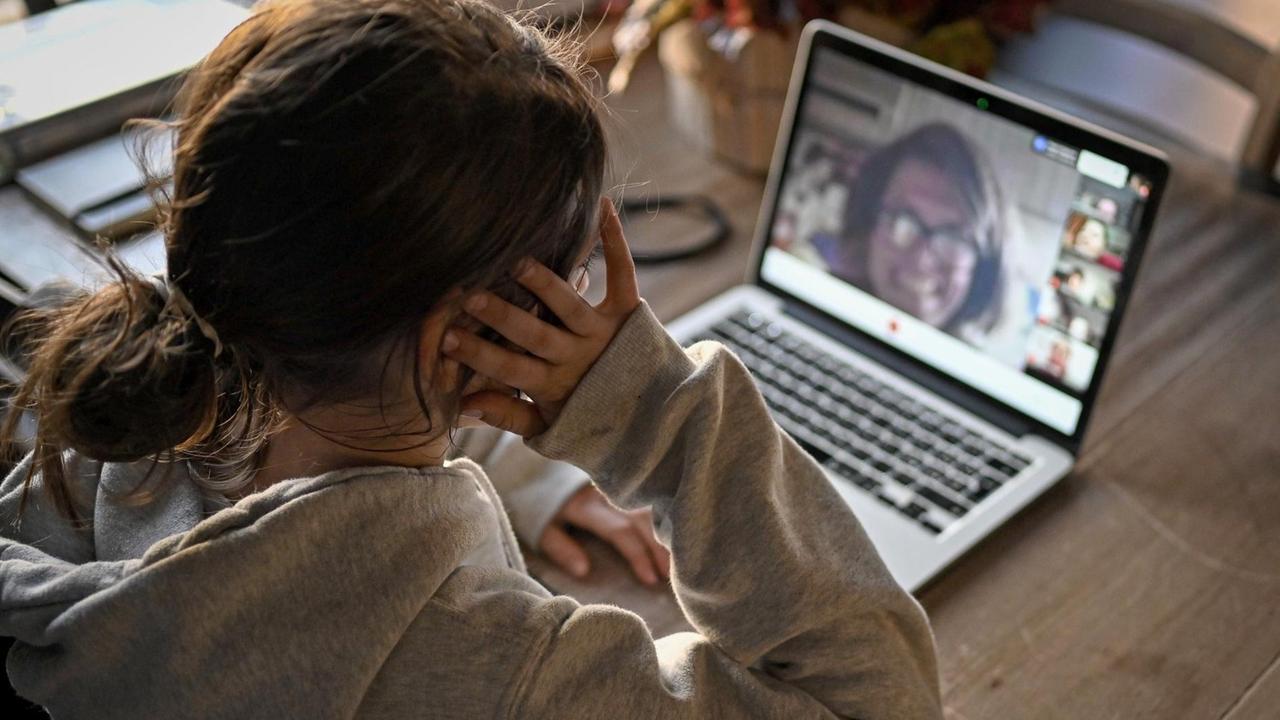 Eine Schülering sitzt am Laptop und unterhält sich mit ihren Schulkameraden und der Lehrerin im gemeinsamen Videochat.