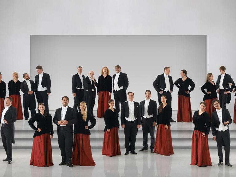 Der Chor steht in schwarz-roter Chorkleidung in einem hellen Raum.