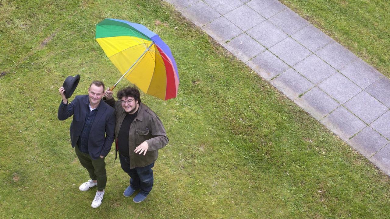 Luftaufnahme von Devid Striesow und Axel Ranisch mit einem bunten Regenschirm. Luftaufnahme von Devid Striesow und Axel Ranisch mit einem bunten Regenschirm.