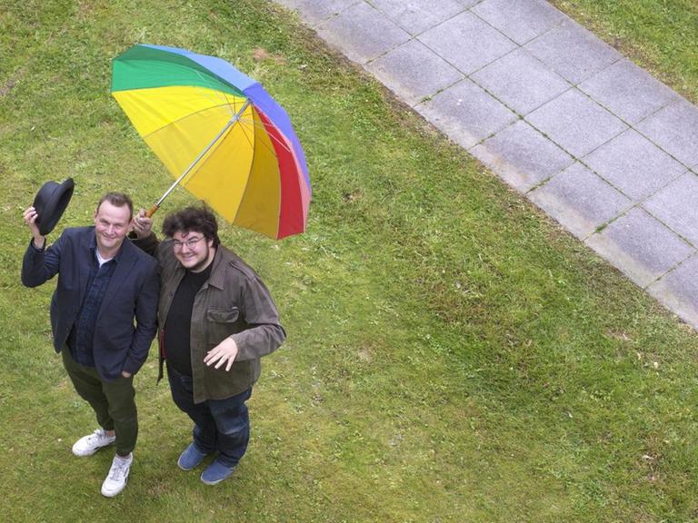 Luftaufnahme von Devid Striesow und Axel Ranisch mit einem bunten Regenschirm.