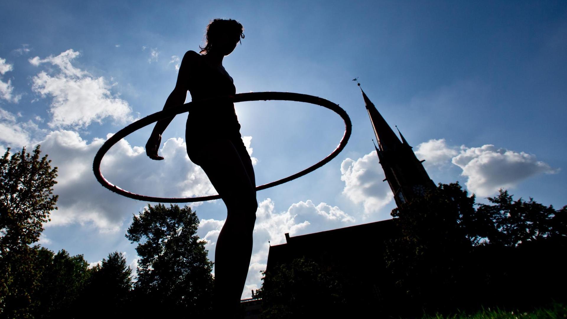 Gegelichtaufnahme einer jungen Frau, die ihren Hula-Hoop-Reifen schwingt. Foto: Daniel Karmann/dpa +++ dpa-Bildfunk +++ Gegelichtaufnahme einer jungen Frau, die ihren Hula-Hoop-Reifen schwingt. Foto: Daniel Karmann/dpa +++ dpa-Bildfunk +++