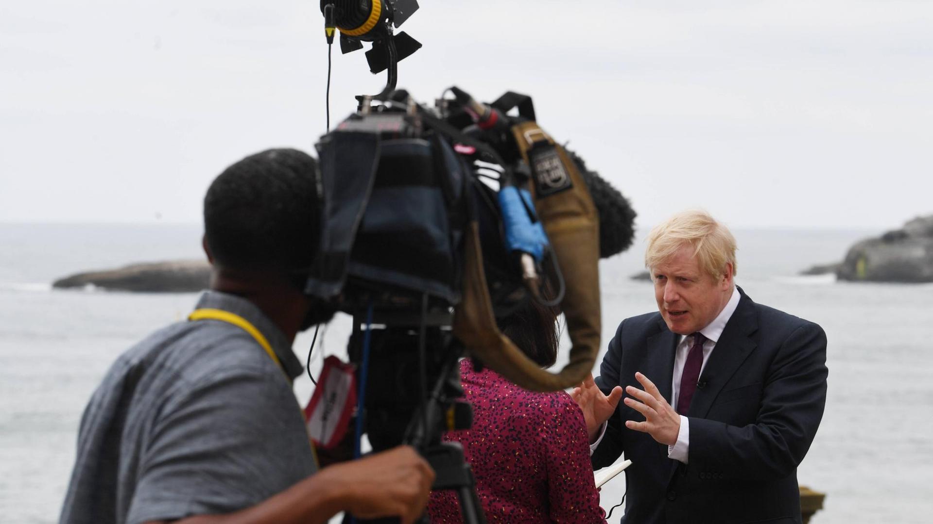 Boris Johnson steht während eines Interviews auf einer Terrasse oberhalb des Meeres und wird von einer Kamera gefilmt. Boris Johnson steht während eines Interviews auf einer Terrasse oberhalb des Meeres und wird von einer Kamera gefilmt.