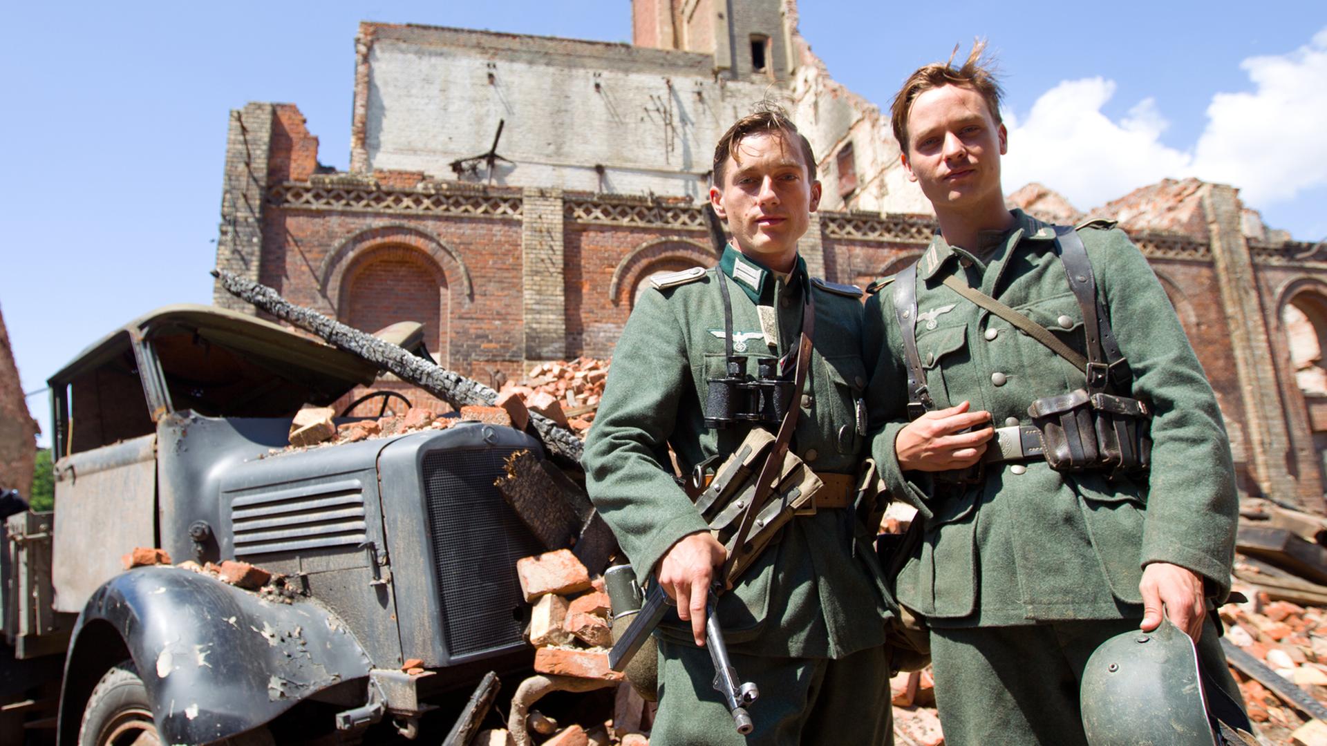 Die Schauspieler Volker Bruch und Tom Schilling stehen bei den Dreharbeiten für den Film "Unsere Mütter, unsere Väter" nebeneinander. Die Schauspieler Volker Bruch und Tom Schilling stehen bei den Dreharbeiten für den Film "Unsere Mütter, unsere Väter" nebeneinander.