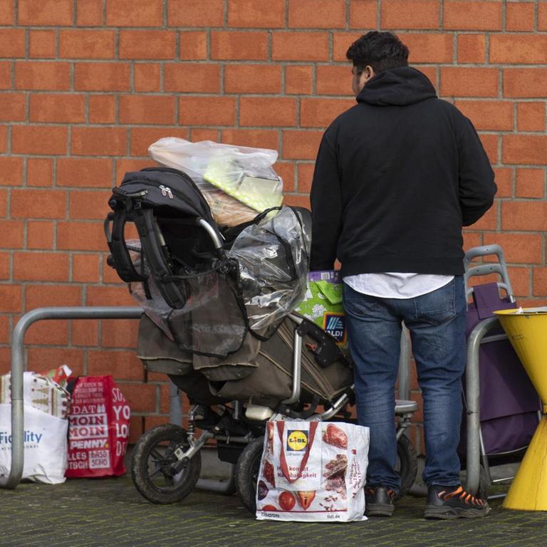 Nachdem sie sich bei der Tafel in der Kirche St. Lioba mit Nahrungsmitteln versorgt haben stehen ein Mann und ein kleines Kind mit vollgepackten Tüten im Freien. Zu den Kunden der Tafeln gehören neben Rentnern auch ganze Familien und alleinstehende Frauen mit ihren Kindern. 