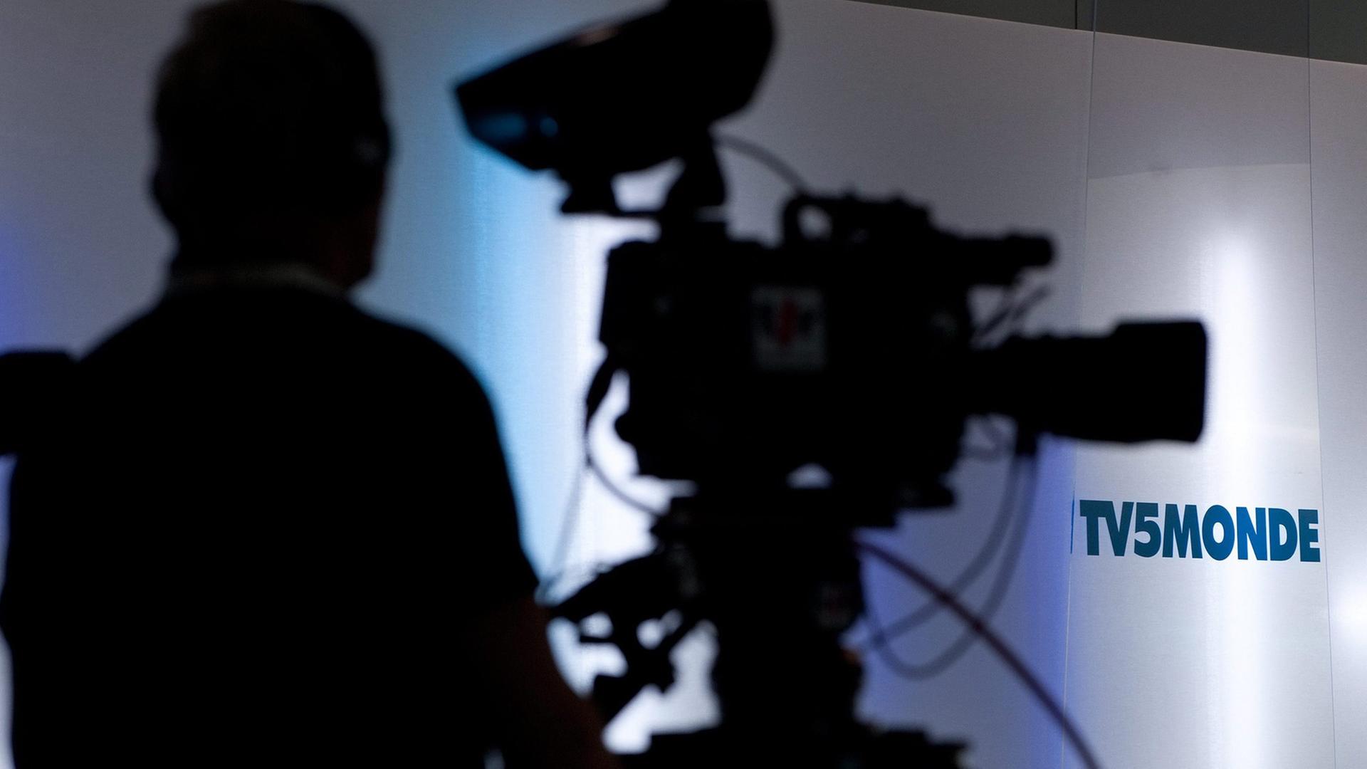 Schattenriss einer Fernsehkamera und ihres Kameramanns vor einer weißen Wand mit dem Logo von TV5 Monde.