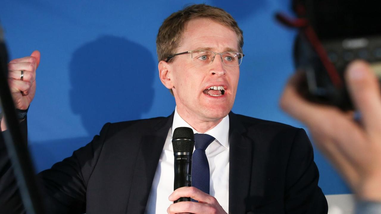 Günther auf der Bühne vor Kameras, mit Mikrofon in der Hand und gestikulierend. Günther auf der Bühne vor Kameras, mit Mikrofon in der Hand und gestikulierend.