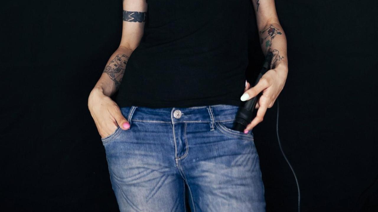 Frau mit rot gefärbten Haaren und Tattoos und Händen in den Taschen ihrer Jeans