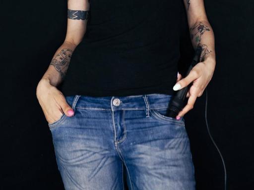 Frau mit rot gefärbten Haaren und Tattoos und Händen in den Taschen ihrer Jeans