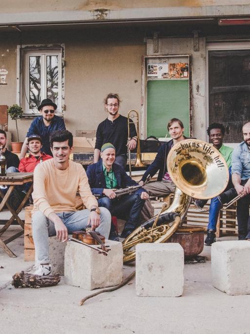 Ein Foto der 'Banda Internationale' aus Dresden, eine Band mit Musiker*innen aus unterschiedlichen Ländern. Sie sitzen mit ihren Instrumenten auf einem Hinterhof.