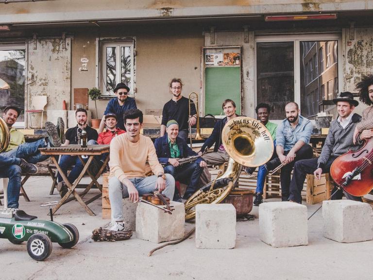 Ein Foto der 'Banda Internationale' aus Dresden, eine Band mit Musiker*innen aus unterschiedlichen Ländern. Sie sitzen mit ihren Instrumenten auf einem Hinterhof.