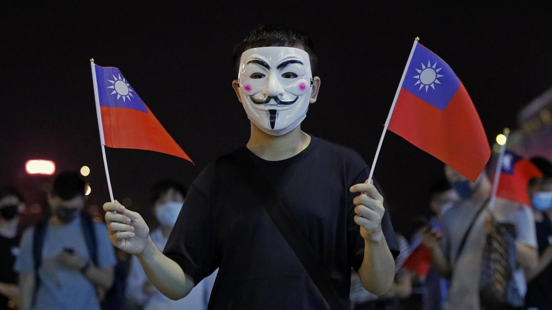 Ein maskierter Mann hält in beiden Händen kleine Taiwan-Flaggen Ein maskierter Mann hält in beiden Händen kleine Taiwan-Flaggen