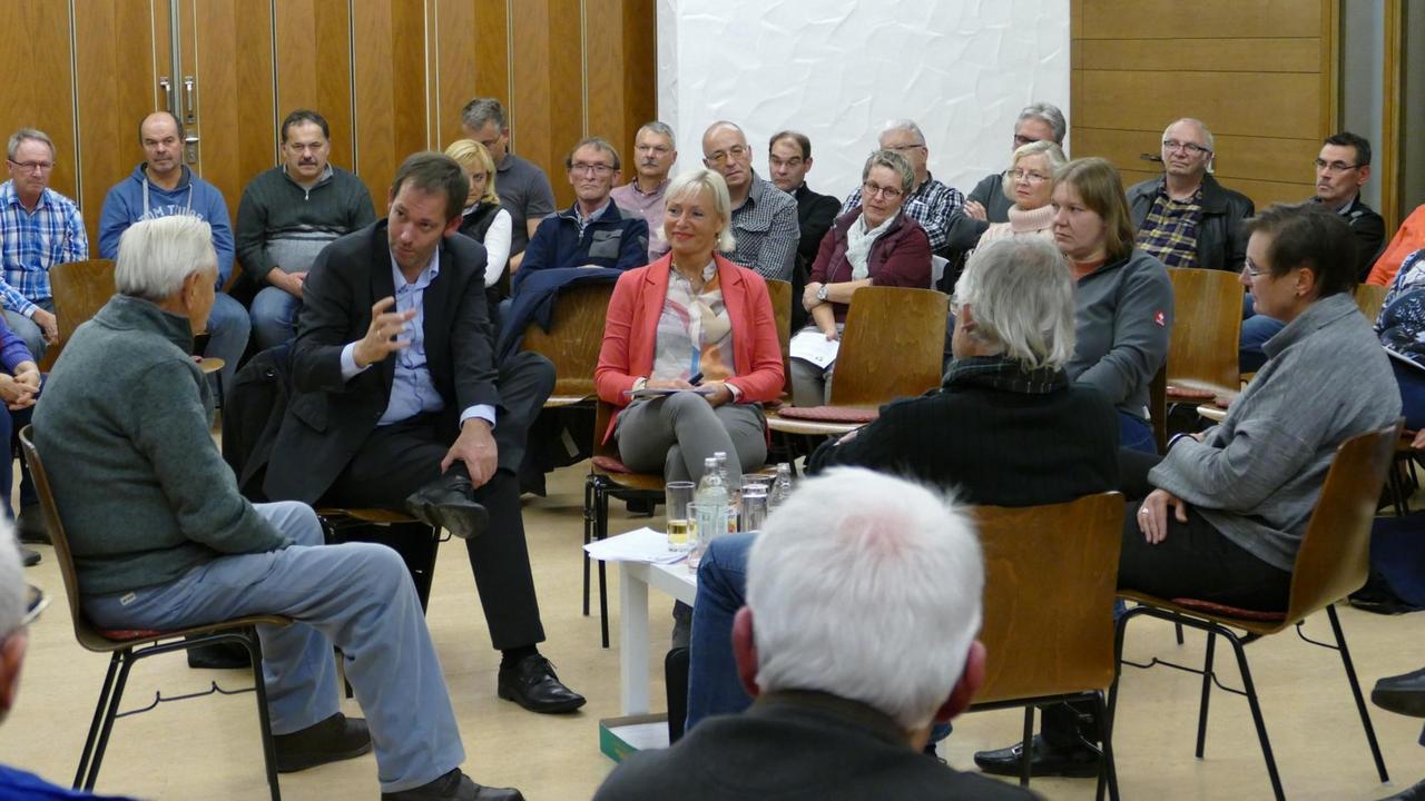 Diverse Bürger sitzen in einem Raum und diskutieren miteinander. Diverse Bürger sitzen in einem Raum und diskutieren miteinander.