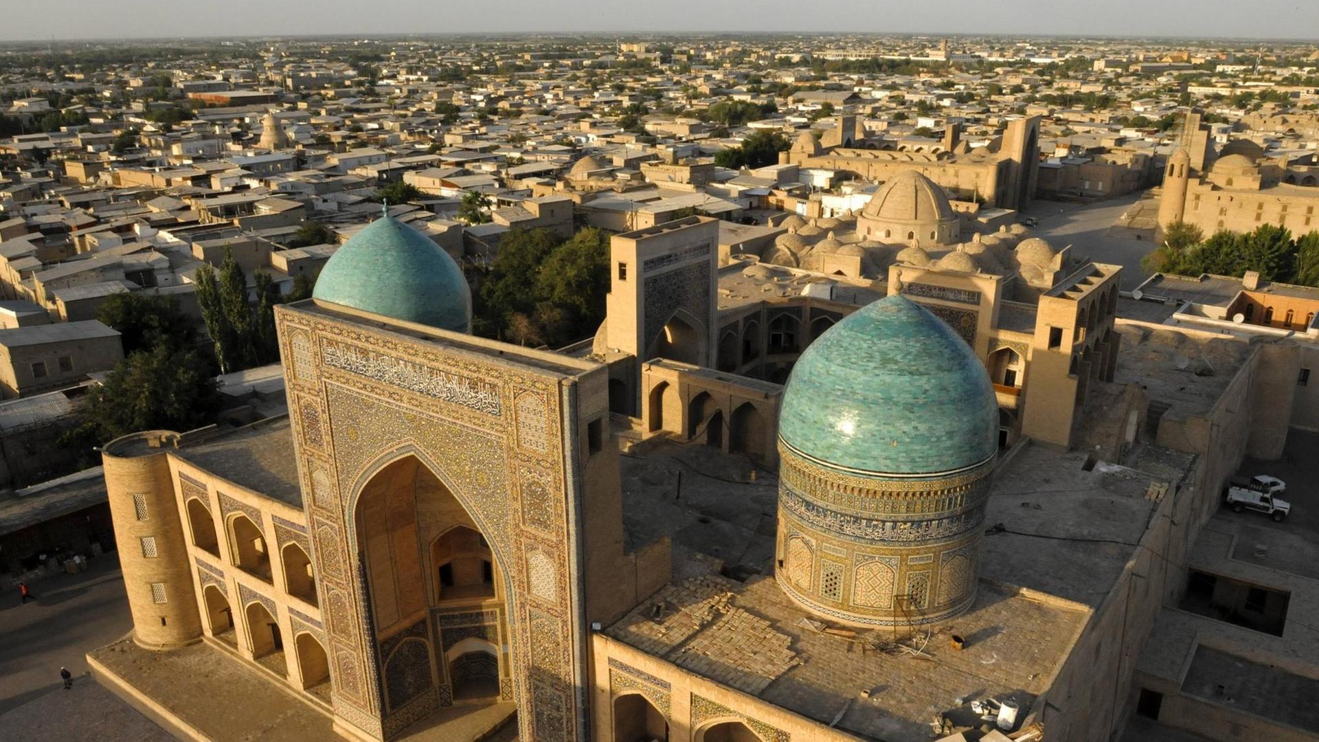 Blick auf die blauen Kuppeln und den großen Iwan der islamischen Lehrstätte Mir-i Arab Madrasa in Usbekistan.