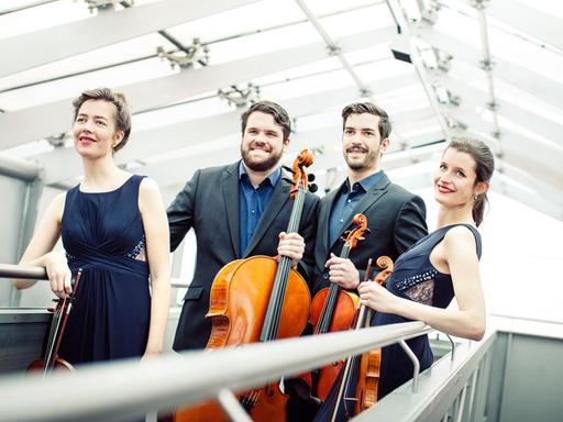 Die vier Musiker des Aris Quartett stehen unter einem Glasdach auf einer Rampe und halten die Instrumente in ihren Händen.