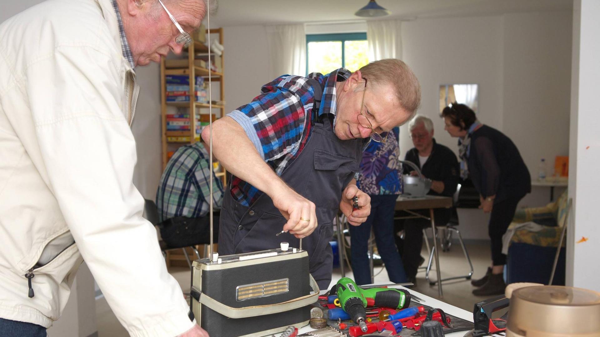 Ein Mann repariert ein altes Radio bei einem Repair Café Treffen. Repair Cafés sind ehrenamtliche Treffen, bei denen die Teilnehmer alleine oder gemeinsam mit anderen ihre kaputten Dinge reparieren. Ein Mann repariert ein altes Radio bei einem Repair Café Treffen. Repair Cafés sind ehrenamtliche Treffen, bei denen die Teilnehmer alleine oder gemeinsam mit anderen ihre kaputten Dinge reparieren.