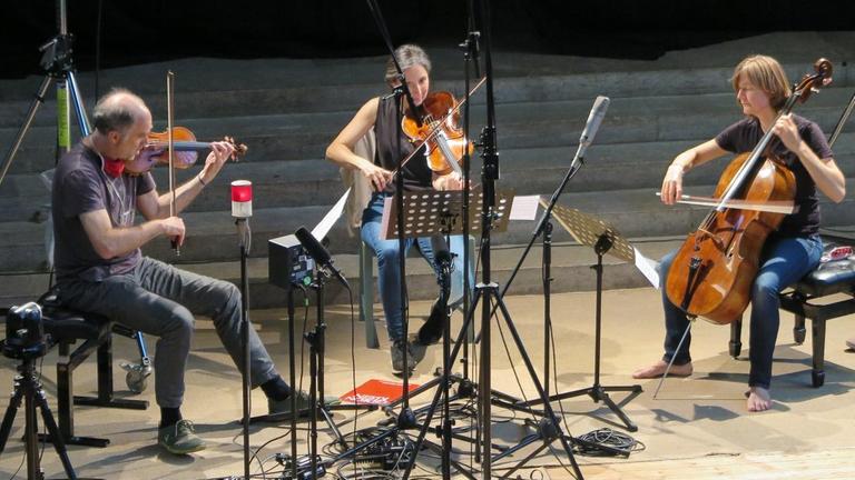 Geiger, Bratschistin und Cellistin spielen vor Mikrofonen ein Radiokonzert Geiger, Bratschistin und Cellistin spielen vor Mikrofonen ein Radiokonzert