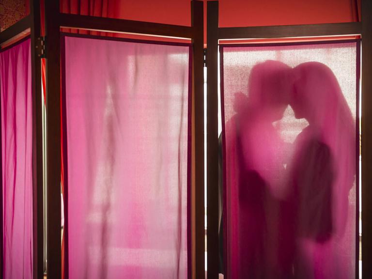 Ein Mann und eine Frau umarmen sich hinter einem durchscheinenden Wandschirm.