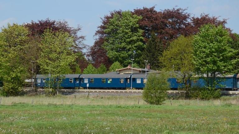 Der blaue Zug des Theaterprojekts "Das letzte Kleinod" fährt durch grüne Landschaft. Der blaue Zug des Theaterprojekts "Das letzte Kleinod" fährt durch grüne Landschaft.