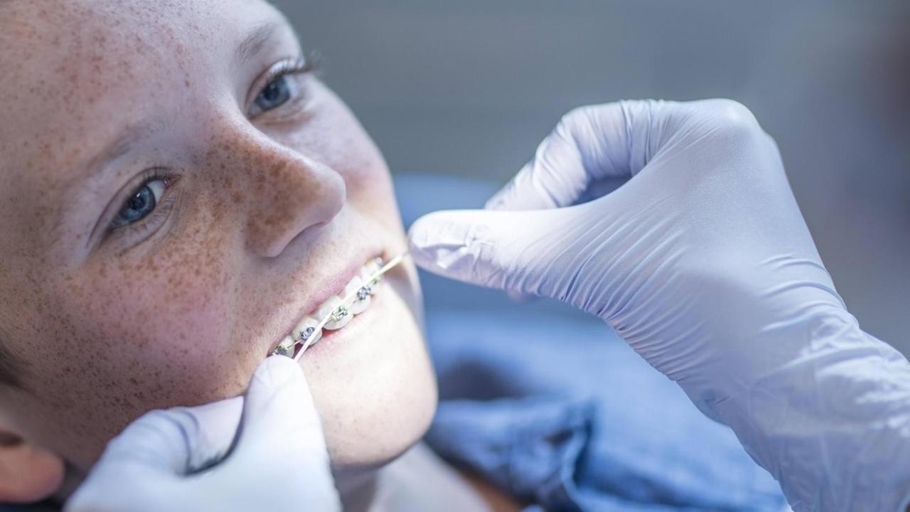 Ein Junge sitzt auf einem Zahnarztstuhl, seine Zahnspange wird gereinigt.