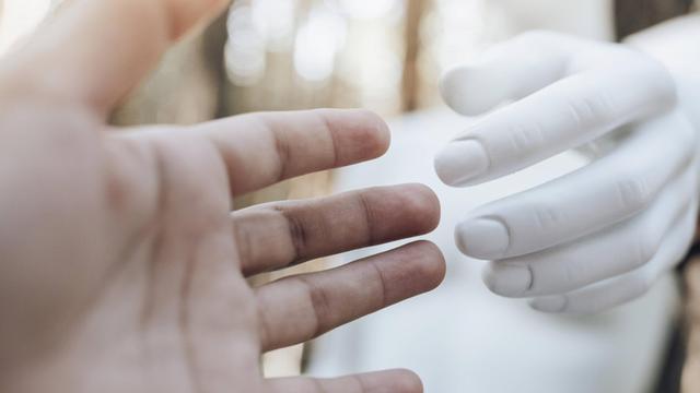 Die Hand einer Frau ist in Richtung der Hand eines Roboters ausgestreckt