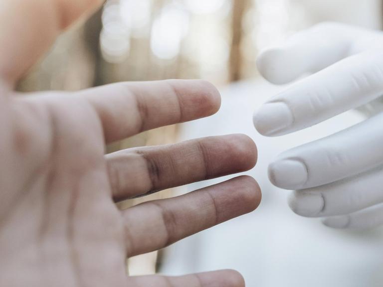 Die Hand einer Frau ist in Richtung der Hand eines Roboters ausgestreckt