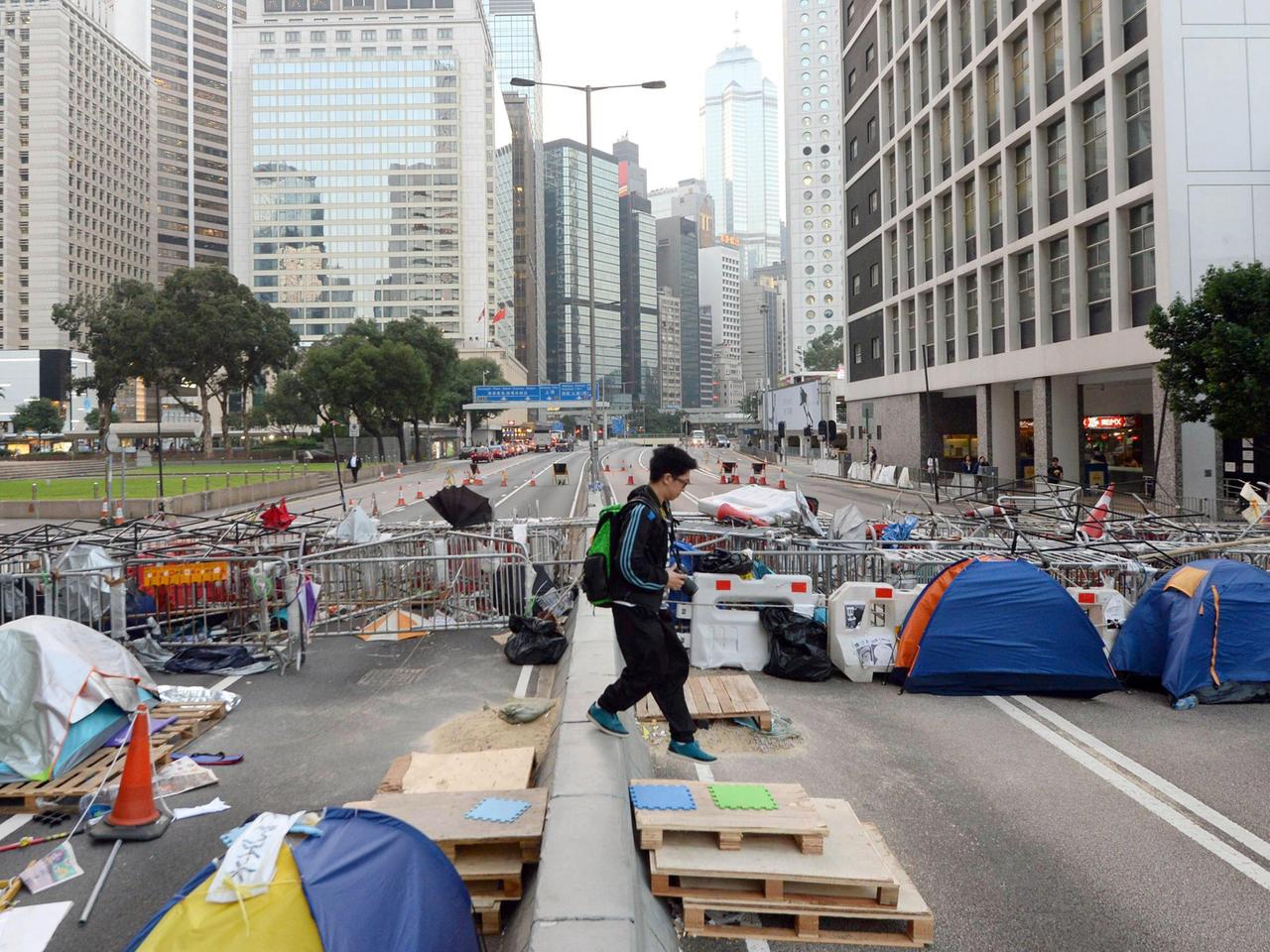 Metallzäune, Paletten und Zelte blockieren eine sechsspurige Straße zwischen Hochhäusern.