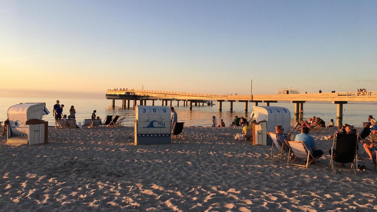 Touristen im Sonnenuntergang sitzen in Liegestühlen am Strand.