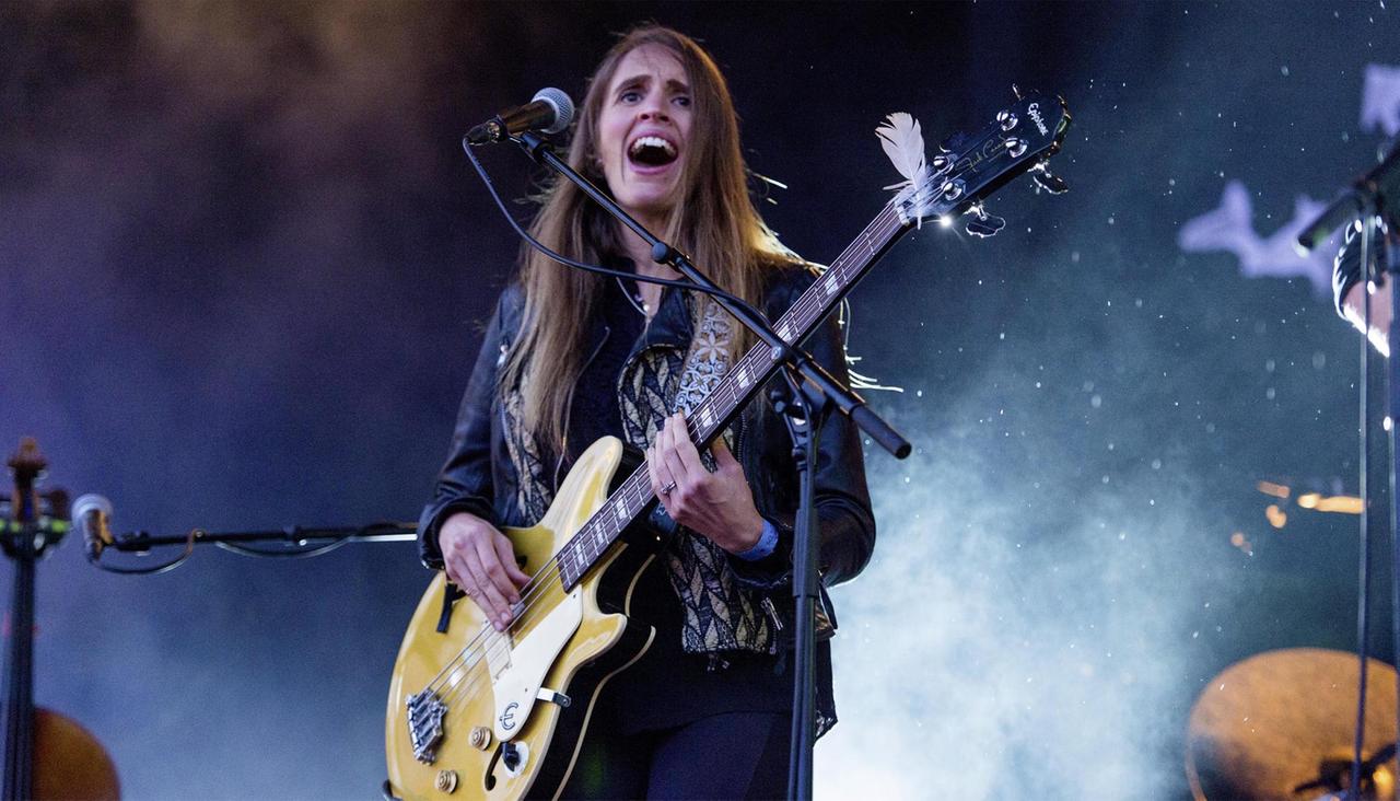 Eine Frau steht mit einer Gitarre auf einer Bühne. Die Bühne ist blau ausgeleuchtet. Eine Frau steht mit einer Gitarre auf einer Bühne. Die Bühne ist blau ausgeleuchtet.