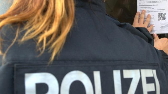Eine Polizistin klebt am 27.10.2015 in Berlin ein Flugblatt mit dem Foto eines Mannes an eine Haustür.