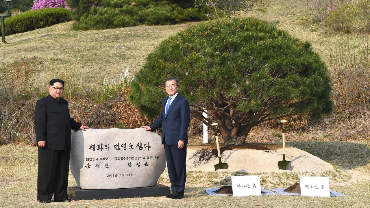 Moon und Kim posieren neben dem Baum und halten ein Banner mit der Aufschrift "Frieden und Wohlstand werden gepflanzt" Moon und Kim posieren neben dem Baum und halten ein Banner mit der Aufschrift "Frieden und Wohlstand werden gepflanzt"