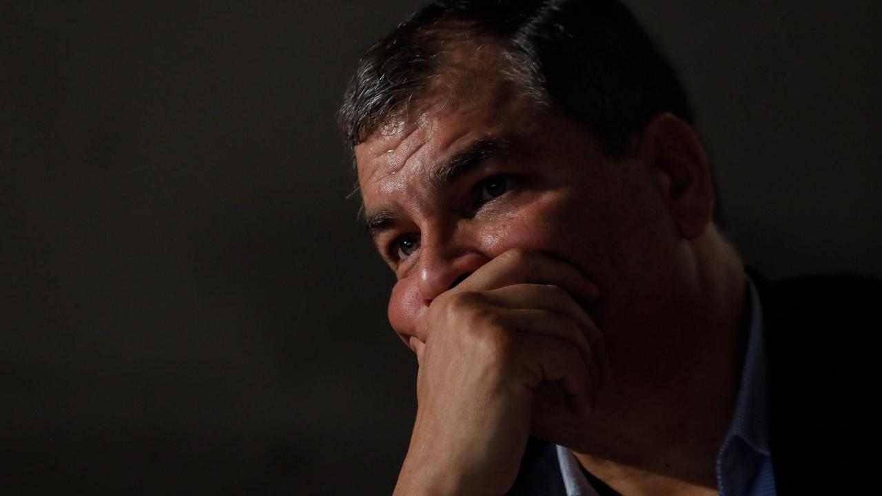 Rafael Correa blickt in einem düster gehaltenen Bild ernst ins Off und hat dabei die Hand vor der Mundpartie.