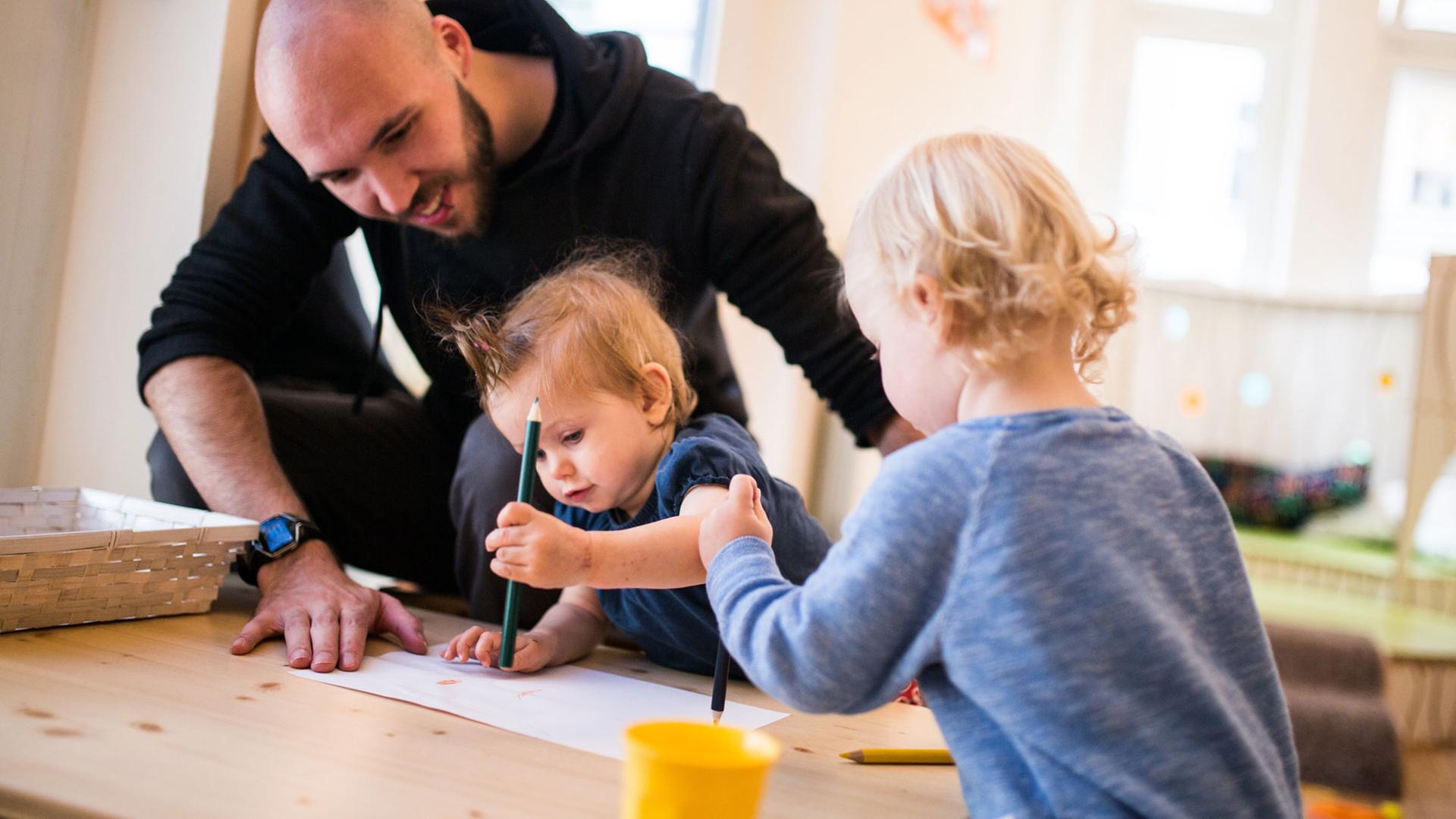 Ein Erzieher malt am 07.07.2016 mit zwei Kindern in der Kindertagesstätte «Coworking Toddler» in Berlin ein Bild. Es begann mit einer Kampagne im Internet, jetzt startet das Projekt «Coworking Toddler» durch. Das Konzept will Eltern dabei helfen, Job und Familie besser zu vereinbaren.