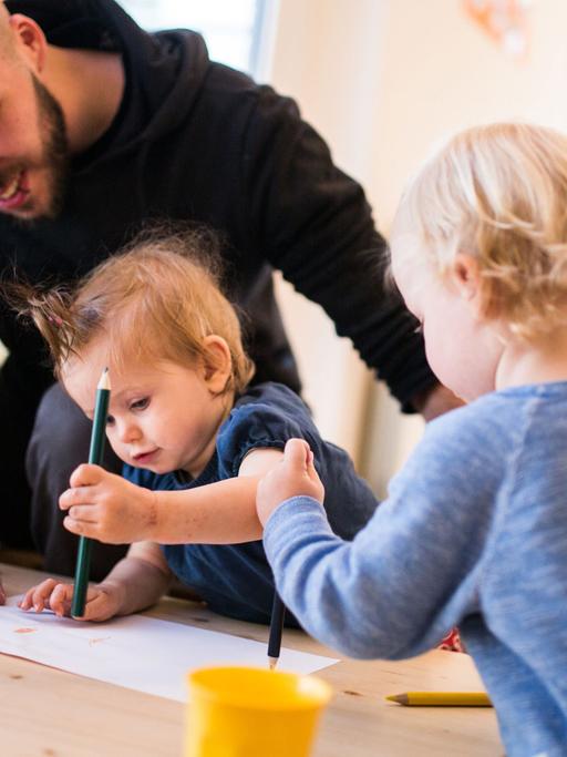 Ein Erzieher malt am 07.07.2016 mit zwei Kindern in der Kindertagesstätte «Coworking Toddler» in Berlin ein Bild. Es begann mit einer Kampagne im Internet, jetzt startet das Projekt «Coworking Toddler» durch. Das Konzept will Eltern dabei helfen, Job und Familie besser zu vereinbaren.