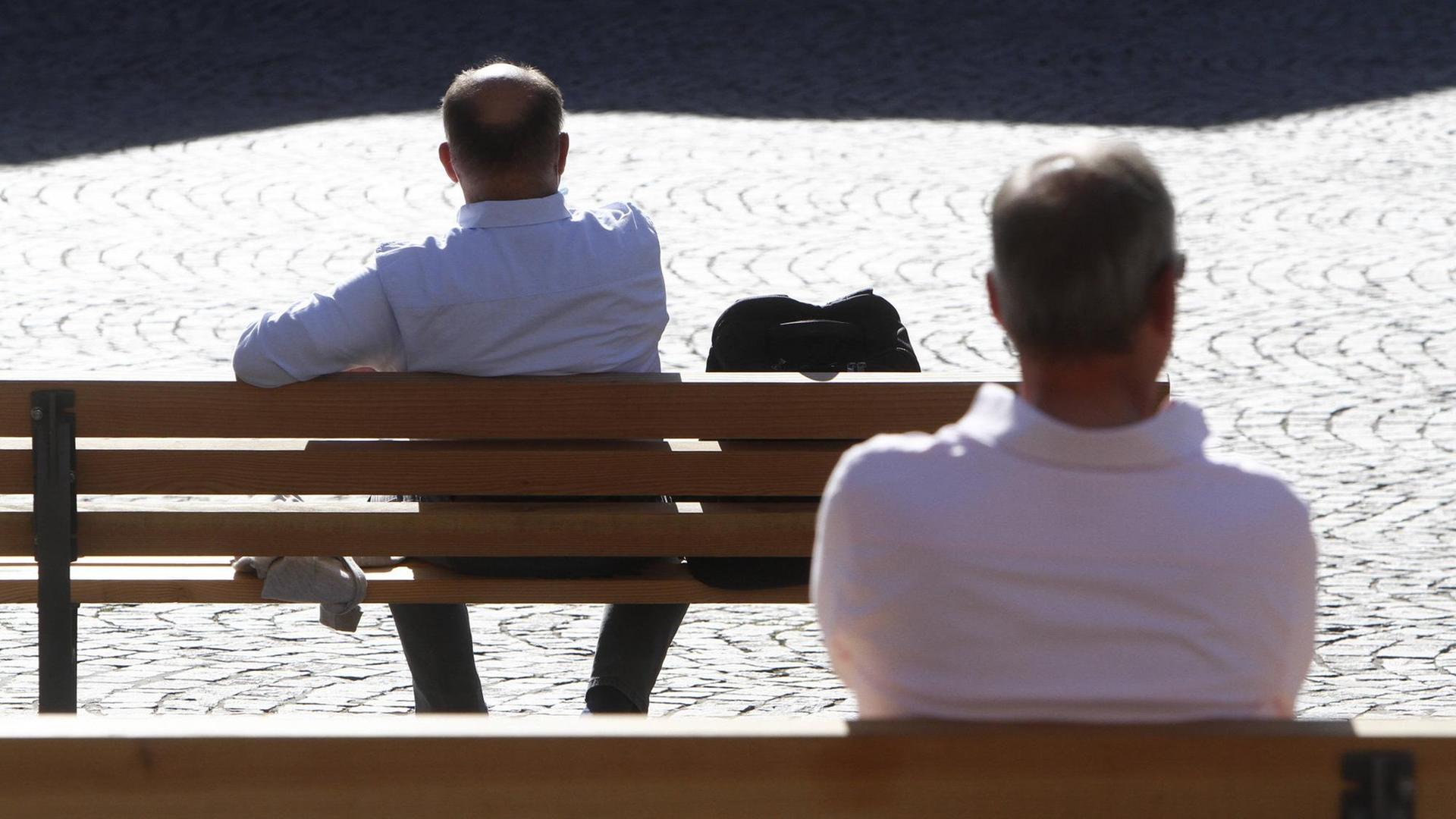 Zwei Männer sitzen einzeln auf zwei Bänken. Zwei Männer sitzen einzeln auf zwei Bänken.
