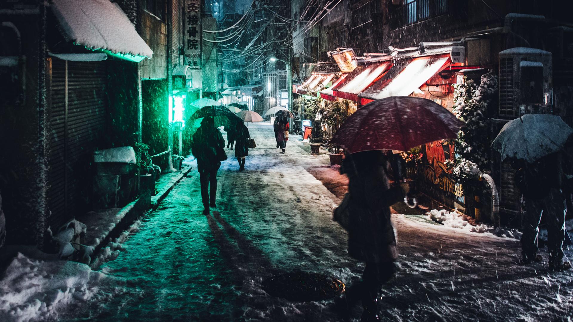 Menschen mit Regenschirmen gehen abends im Schirm durch eine kleine Straße in Tokio. Menschen mit Regenschirmen gehen abends im Schirm durch eine kleine Straße in Tokio.