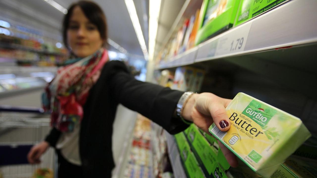 Eine Frau nimmt in einem Supermarkt Bio-Butter aus dem Regal. Eine Frau nimmt in einem Supermarkt Bio-Butter aus dem Regal.